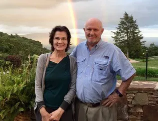 Christie smiling outdoors in the mountains with a rainbow in the sky behind her
